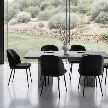 Scarlett Velvet Dining Chair Set of 2 in Black, featuring slim black upholstered chairs with sleek metal legs, around a stone table. They add elegance and comfort to the minimalist dining area.