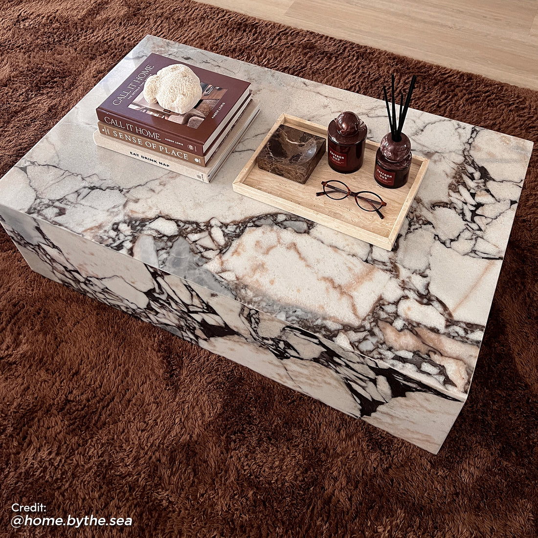 Solene 100cm Coffee Table in Real Blue Galaxy Marble on a brown rug, featuring a marble pattern, books, coral, a tray with red jars, a marble bowl, and reading glasses.