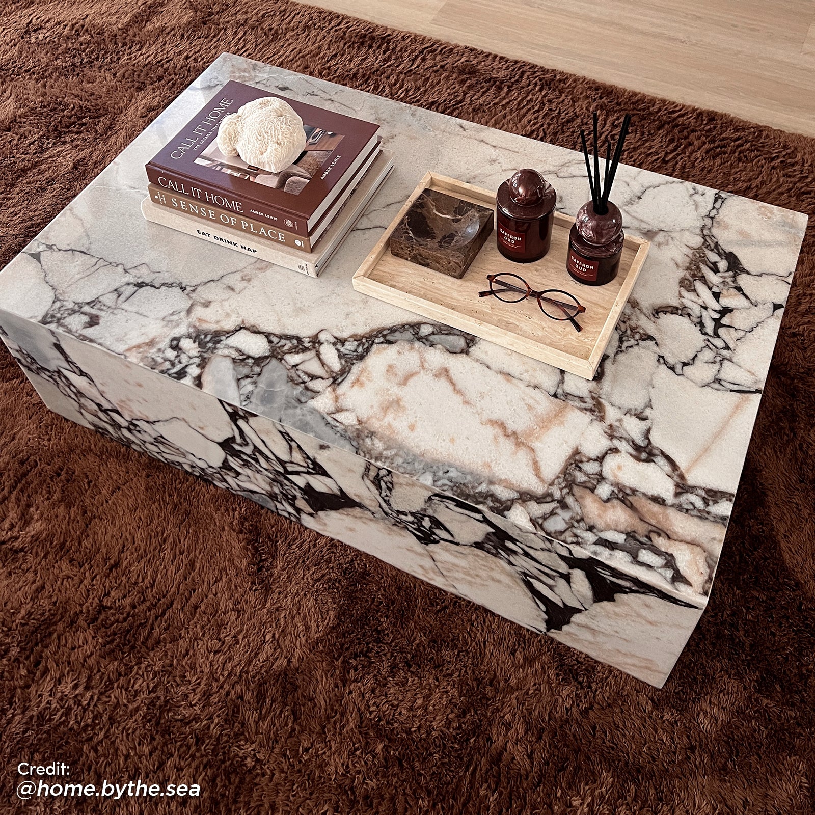 Solene 100cm Coffee Table in Real Blue Galaxy Marble on a brown rug, featuring a marble pattern, books, coral, a tray with red jars, a marble bowl, and reading glasses.