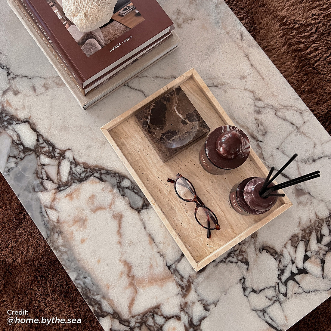 Solene 100cm Coffee Table in Real Blue Galaxy Marble, features a marble top with natural veining, styled with stone accessories, books, and coral on a plush chocolate-brown rug, embodying luxurious elegance.