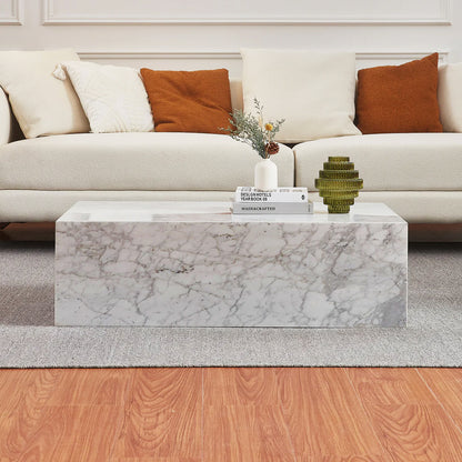 Solene 100cm Coffee Table in Real Carrara Marble features a low rectangular form with distinctive veining, surrounded by books, a vase, and a vessel, enhancing a modern living-room vignette.