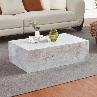 Solene 100cm Coffee Table in Real Carrara Marble, showcased with natural veining and a clean, low-profile design, accompanied by books and vases on a light gray rug in a modern living room.