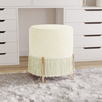 Stacey Tassled Velvet Foot Stool Ottoman in Cream features cream velvet upholstery, fringe tassels, and gold-tone legs, resting on a gray shag rug, enhancing elegance in any space.