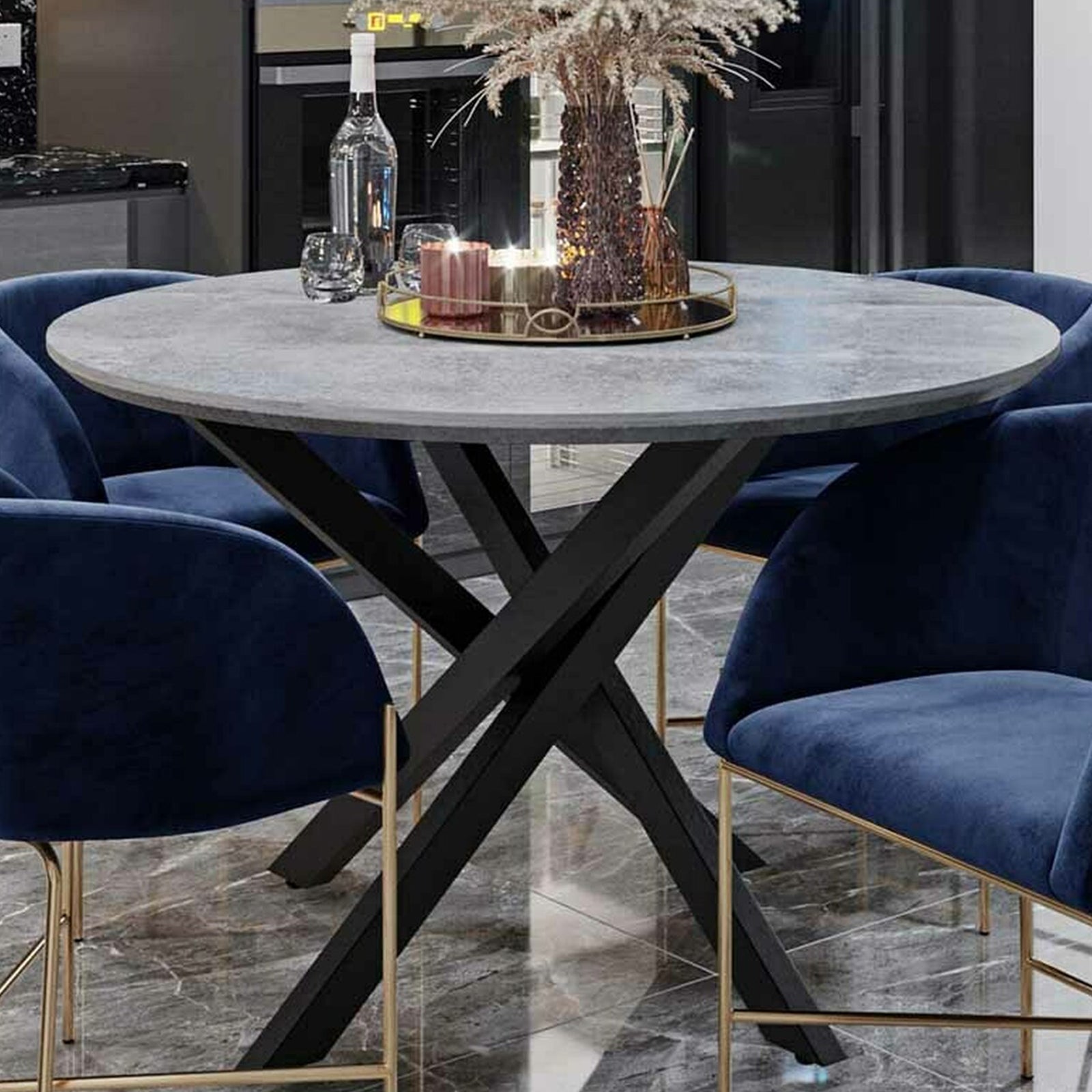 Close-up of the Stoten Round Dining Table Concrete, showcasing its round top with a concrete finish and black powder-coated legs that cross and taper, emphasizing its modern and sturdy design.