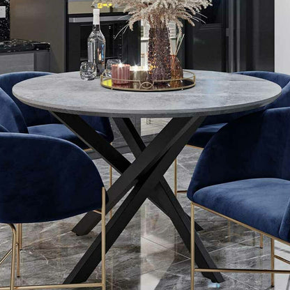 Close-up of the Stoten Round Dining Table Concrete, showcasing its round top with a concrete finish and black powder-coated legs that cross and taper, emphasizing its modern and sturdy design.
