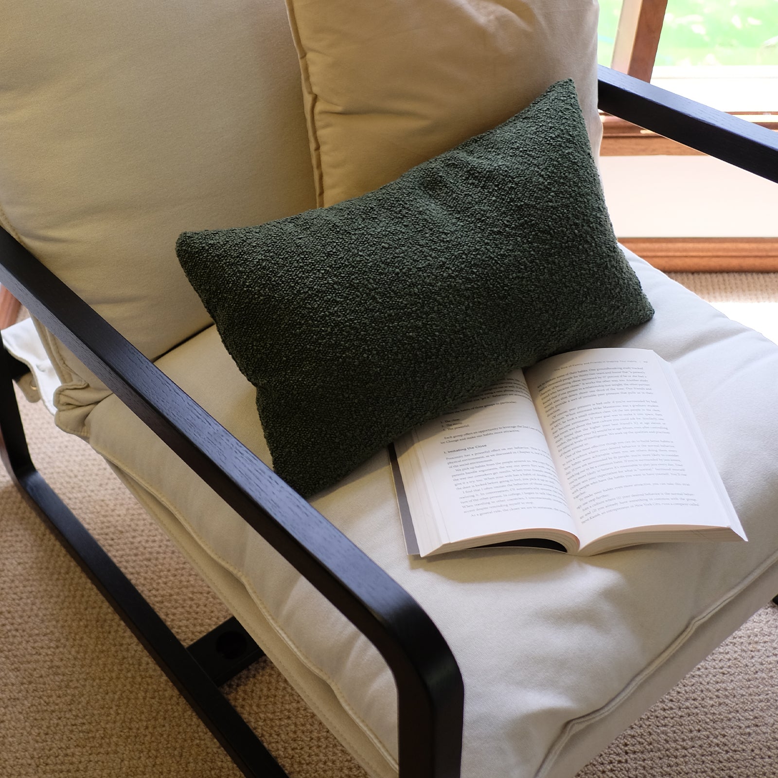 Tilly Linen Hardwood Arm Chair Black with a green throw pillow and book on the seat, showcasing its solid oak frame and plush cushion, epitomizing minimalist comfort and style.
