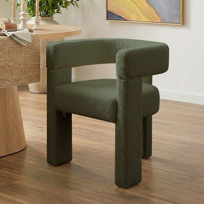 Utah Bouclé Curved 3 Legged Accent Chair in Green with textured upholstery, chunky tubular legs, and a curved backrest, positioned on a wooden floor near a dining table with decor.