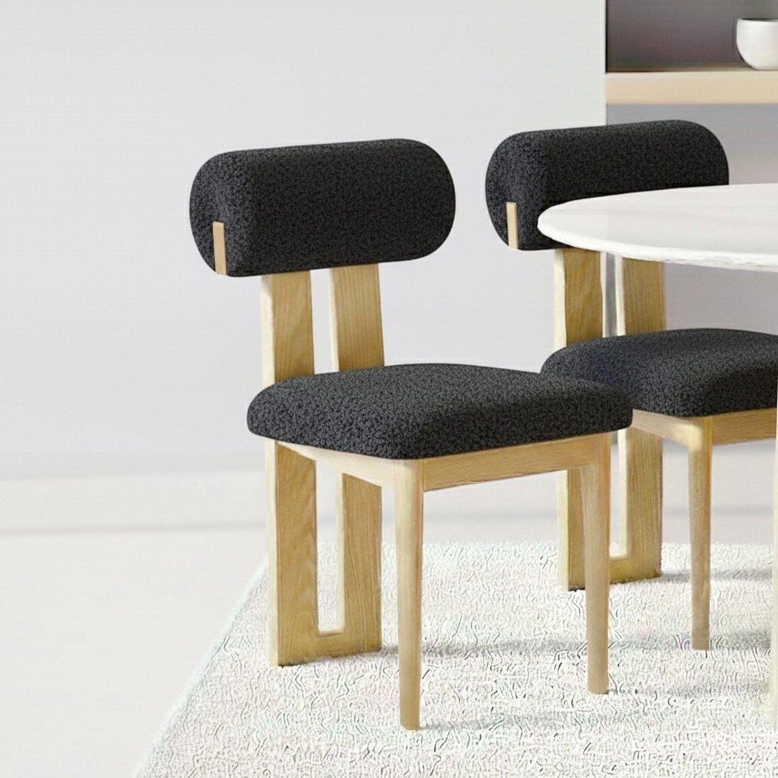 Wylie Boucle Hardwood Oak Dining Chair Set of 2 in Black featuring wooden-frame chairs with rounded-cushion seats and cylindrical backrests, positioned beside a white tabletop on a textured rug.