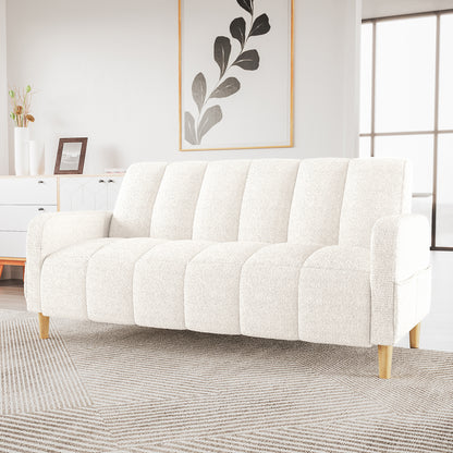 Anica 3 Seater Boucle Sofa Bed in Cream White with vertical channel tufting, light wooden legs, set in a bright room with a patterned rug, white console, and gold-framed botanical print.