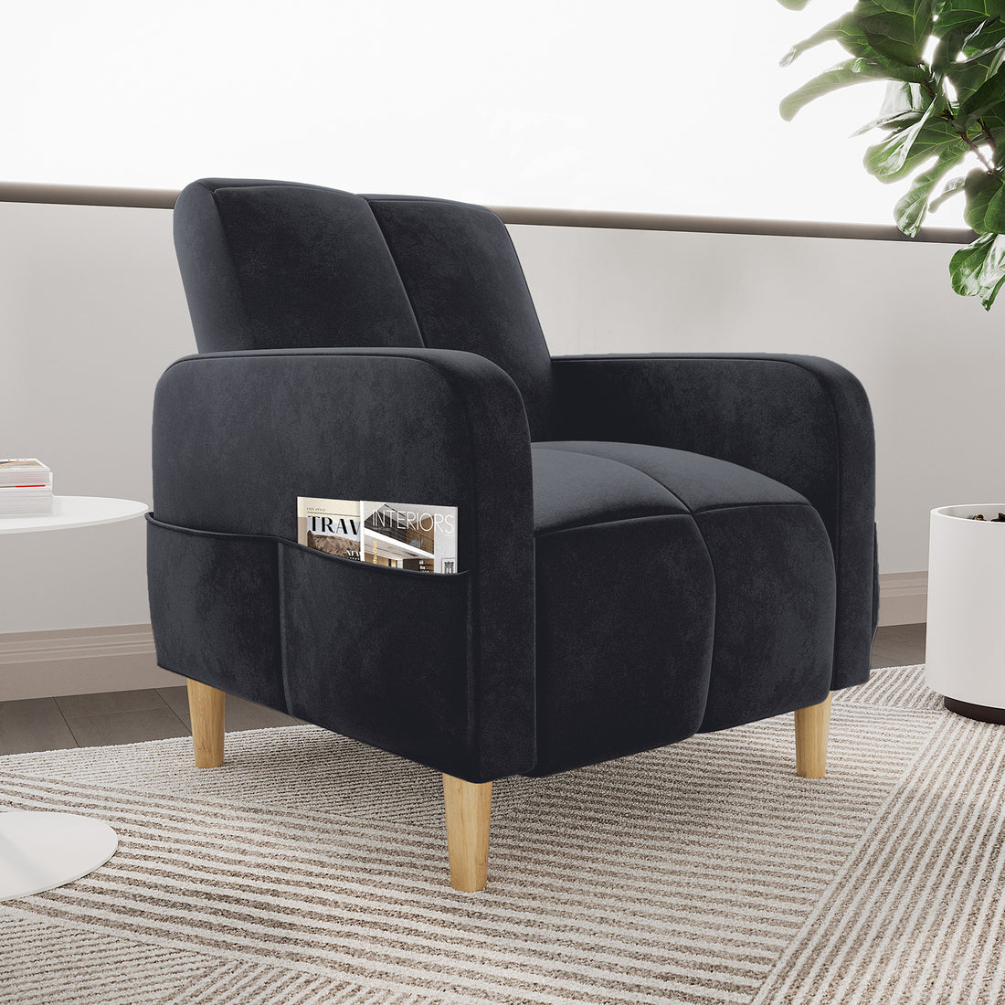 Anica Single Seater Velvet Sofa Chair in Black with rounded arms, divided cushions, light-wood tapered legs, and a side magazine pocket, set on a striped rug beside a white table.