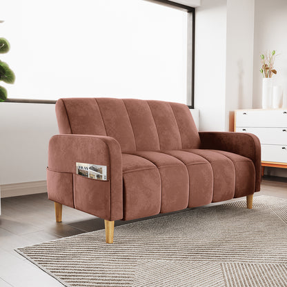 Anica 2 Seater Velvet Fabric Sofa Bed in Blush with channel-stitched cushions, slim curved arms, tapered wooden legs, and a side pocket. It sits on a patterned rug in a modern living room.