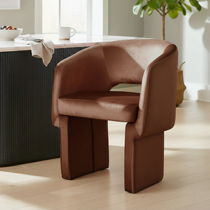 Avela Velvet Fabric Curved Accent Armchair in Mocha Mousse, featuring a sculptural design with plush upholstery and block-like legs, placed in a minimalist corner near a countertop with decor elements.
