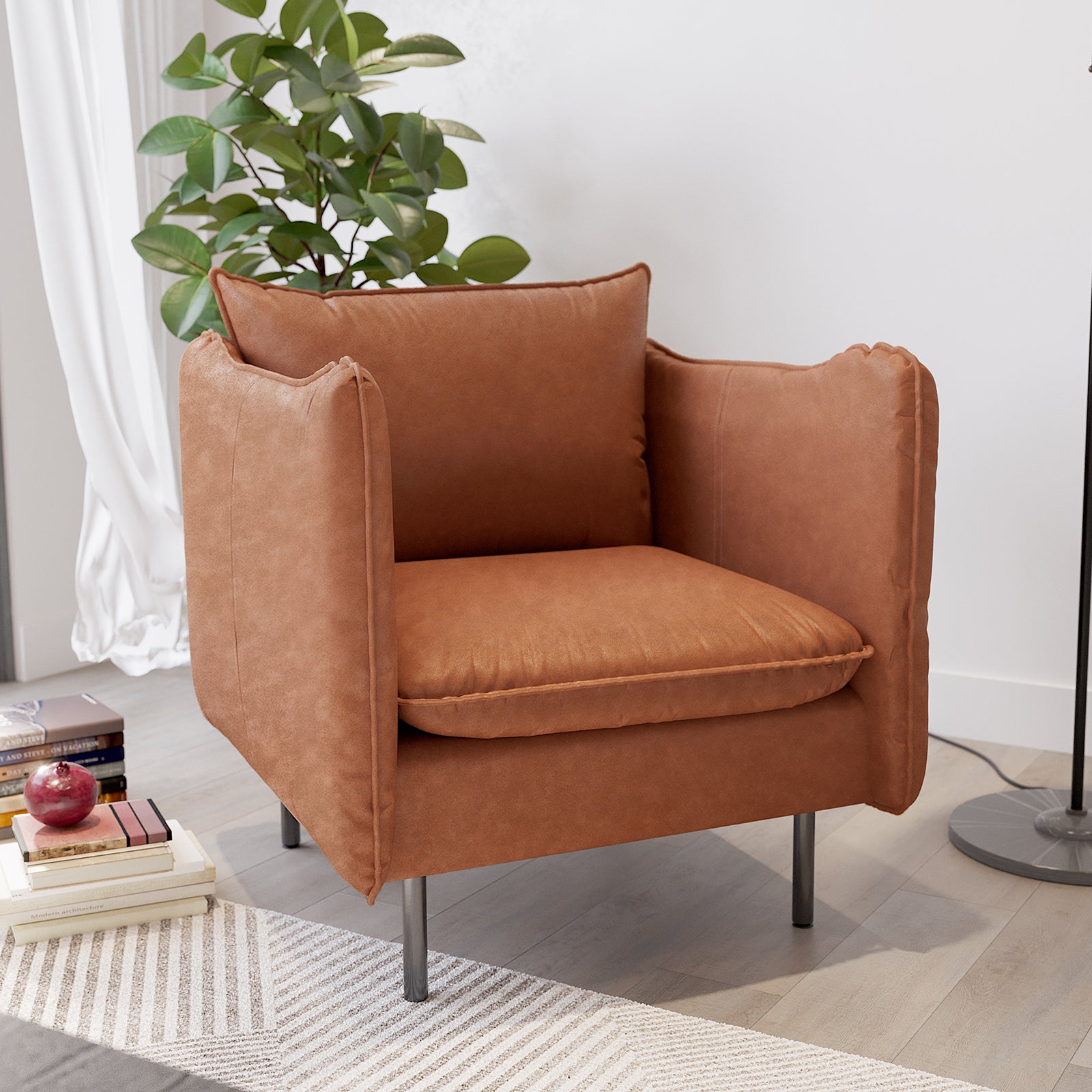 Cassian PU Leather Armchair in Mocha, featuring plush rust-brown upholstery, slim black metal legs, and removable cushions, is placed in a modern setting with a leafy plant and books nearby.