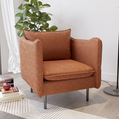 Cassian PU Leather Armchair in Mocha, featuring plush rust-brown upholstery, slim black metal legs, and removable cushions, is placed in a modern setting with a leafy plant and books nearby.