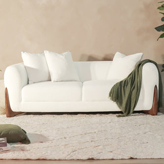 Charla 3-Seater Boucle Sofa with Pillows - Cream White, showcasing a plush, textured fabric and high-density foam cushions, complemented by a green blanket and a white pillow on a white couch.