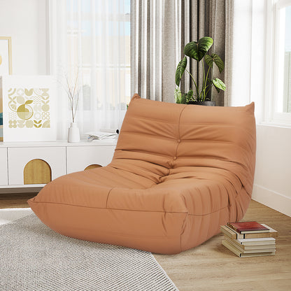 Claris PU Leather Tufted Lounge Sofa Chair in Caramel, featuring a low, slouchy design with warm tan leather, positioned in a bright, modern living room corner with light-wood flooring and a media console.