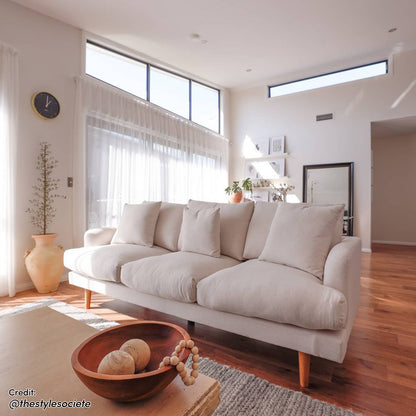 Colton Fabric 3 Seater Sofa Cream White, featuring sleek lines and plush cushions, displayed in an elegant living room setting with a modern indoor plant and stylish pillows.