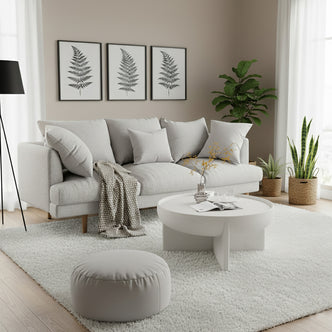 Colton 3-Seater Fabric Sofa in Stone, featuring light-gray upholstery with matching cushions, set in a bright, minimalist living room with botanical prints, a shag rug, and floor-to-ceiling window.