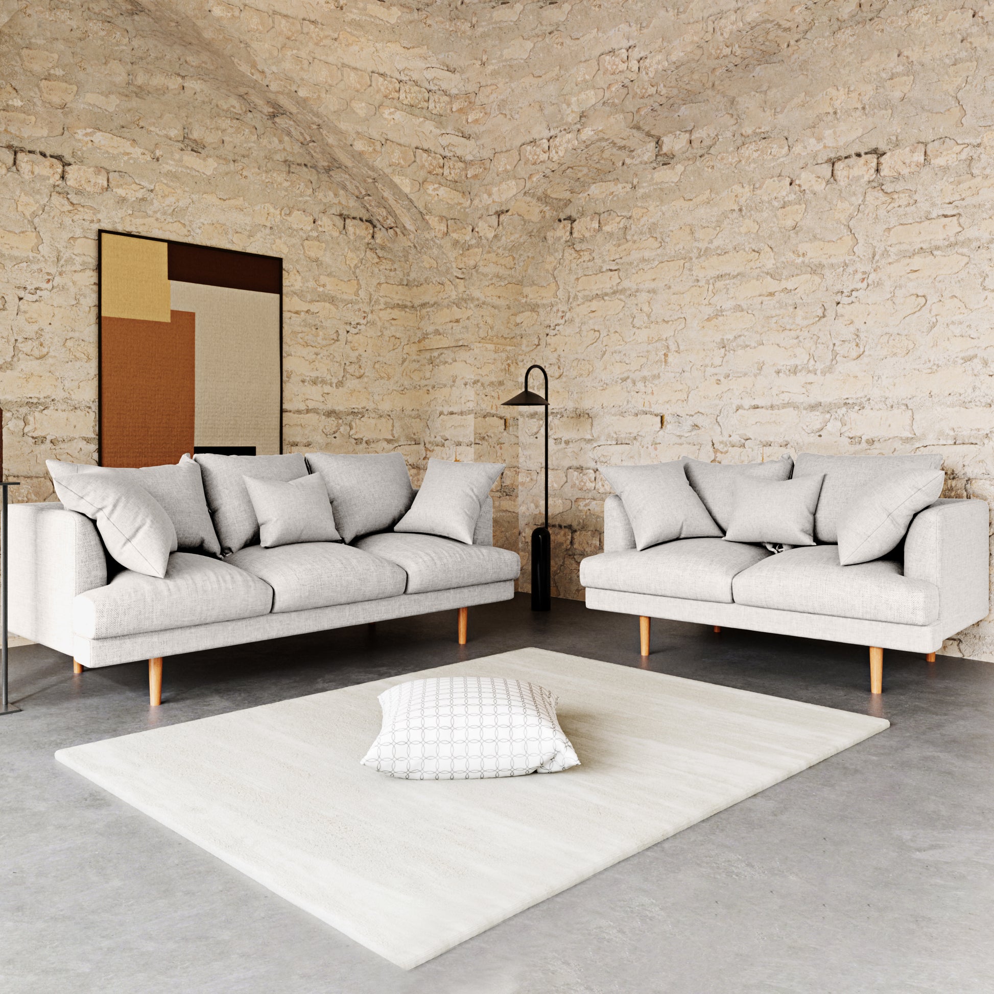 Colton 5-Seater Fabric Sofa in Cream White shown in a minimalist room with mid-century style, featuring a 3-seater and 2-seater sofa with matching pillows, on a concrete floor with an off-white rug.