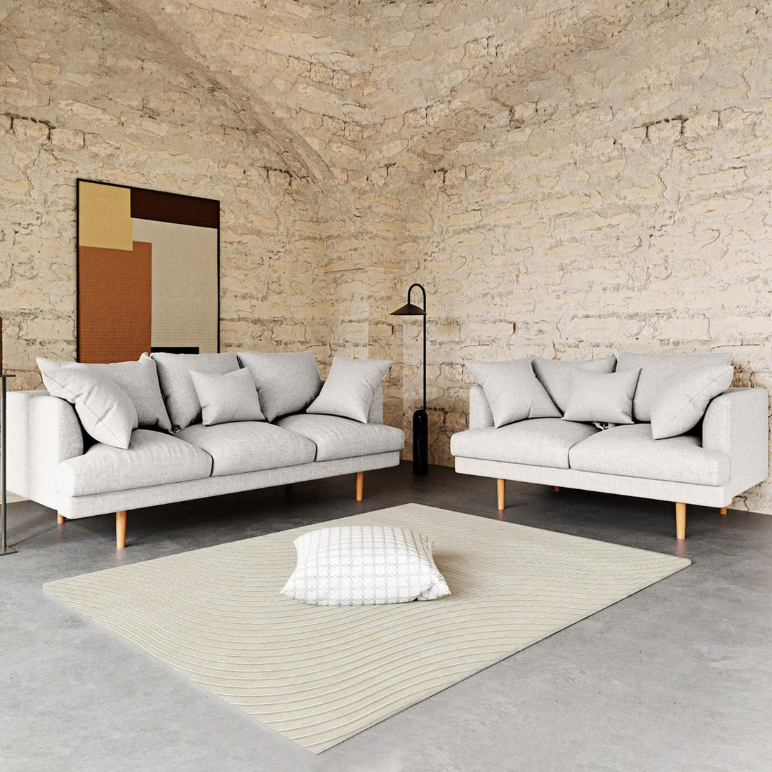 Colton Living Room Package in Cream White featuring two light-gray sofas with accent pillows, a cream-beige rug on concrete, and a black floor lamp, creating a minimalist, industrial-style ambiance.