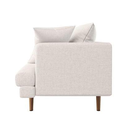 Side profile of the Colton Living Room Package - Cream White, featuring a light-cream upholstered sofa module with two back cushions, low armrest, and slender, tapered wooden legs.