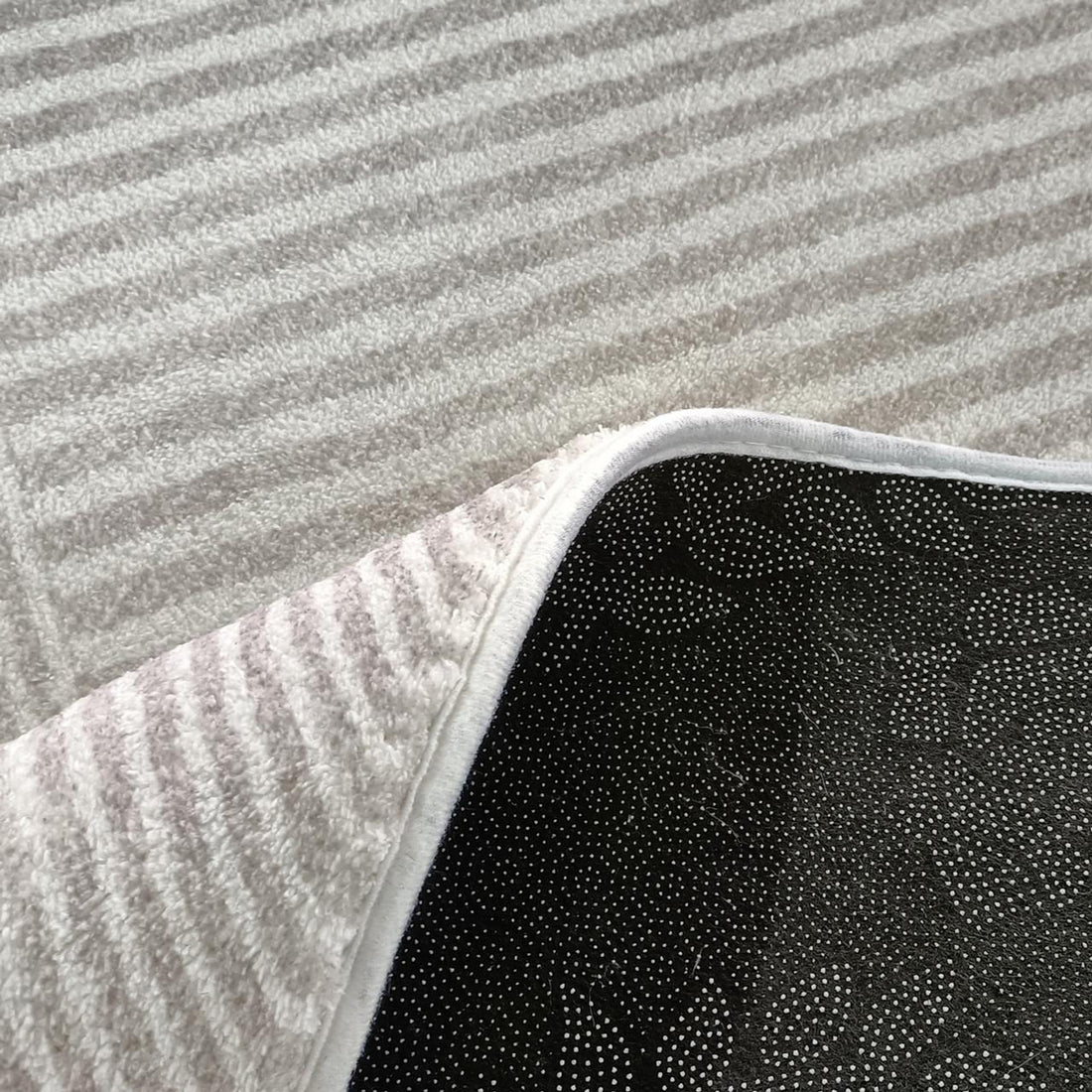 Close-up of Colton Living Room Package - Cream White, showcasing the corner of a white striped terry-cloth rug with a non-slip black rubberized backing on a light-gray carpet.