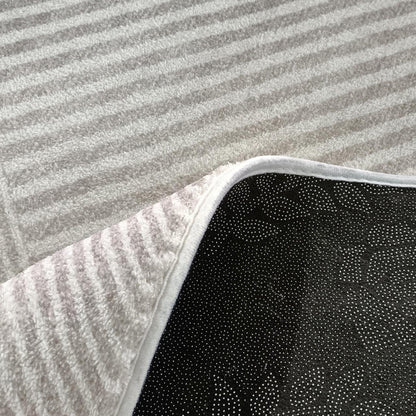 Close-up of Colton Living Room Package - Cream White, showcasing the corner of a white striped terry-cloth rug with a non-slip black rubberized backing on a light-gray carpet.