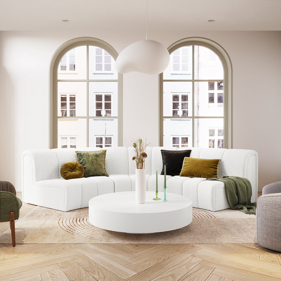 Corina 3 Seater Modular Boucle Sofa in Cream White, L-shaped with muted green and brown accent pillows, green throw, on herringbone wood floor, round coffee table, dried stems, and candles.