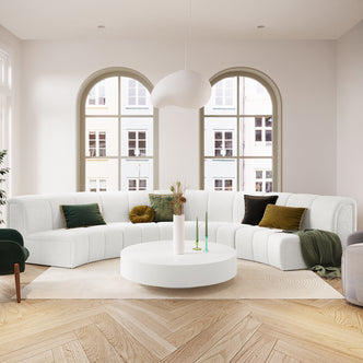 Corina 4 Seater Modular Boucle Sofa in Cream White, featuring a curved design with deep green and mustard accent pillows, set in a bright, minimalist living room with arched windows and parquet flooring.