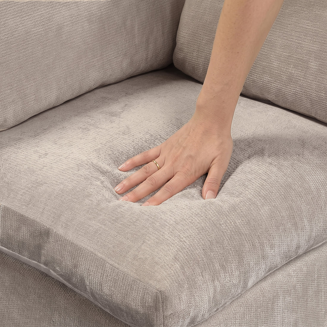 A close-up view of a hand pressing down into the plush, light taupe fabric of a sofa seat cushion, demonstrating its softness and cushioning.