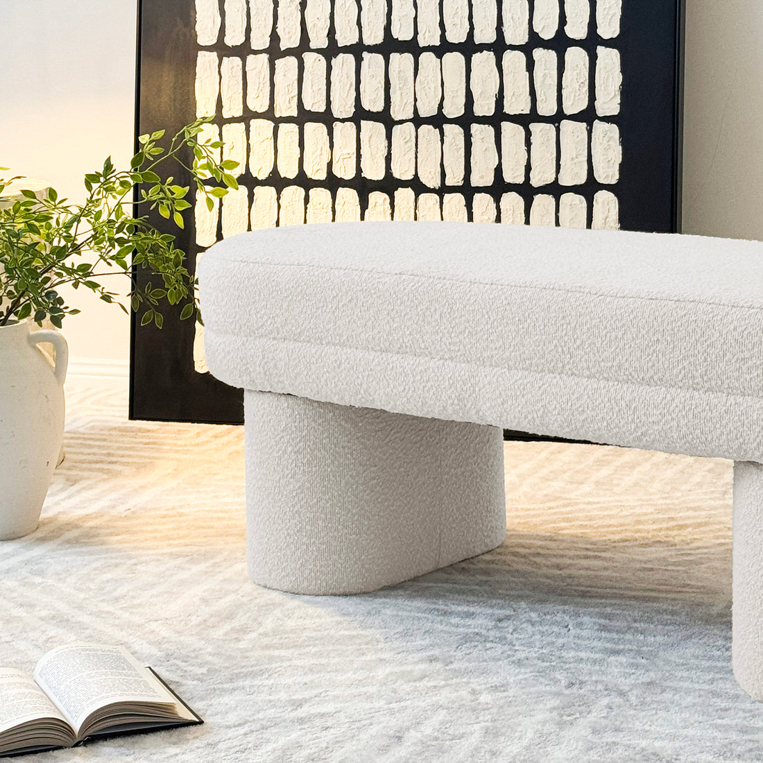 Elzan Bouclé Upholstered Bench features curved design with plush bouclé fabric, creating a modern, elegant look. Positioned on a soft white carpet, enhancing its luxurious appeal in a home setting.