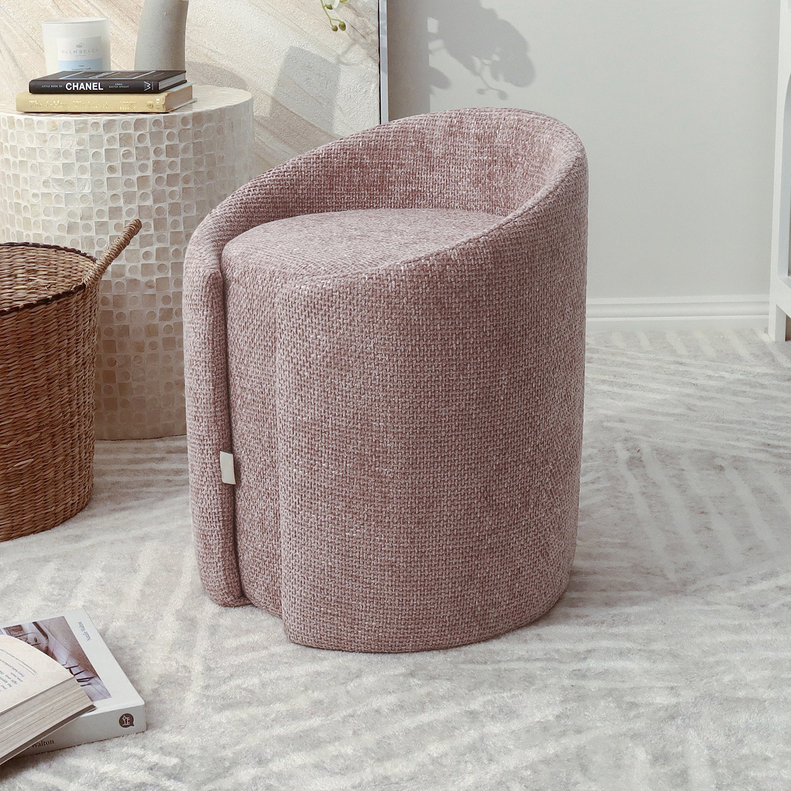 Emiken Chenille Fabric Ottoman Stool in Light Pink, featuring a barrel design with soft chenille upholstery, placed on a patterned rug beside a wicker basket and mosaic-style table in a minimalist room.