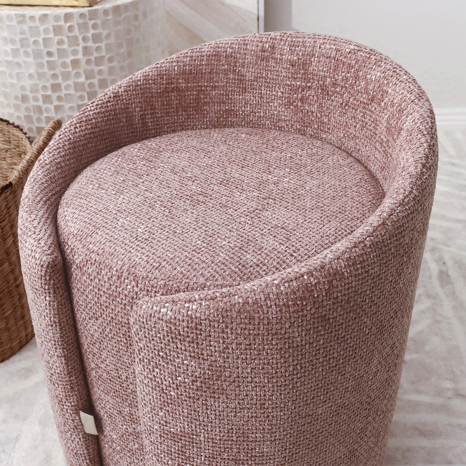 Emiken Chenille Fabric Ottoman Stool in Light Pink, featuring a round, barrel-style design with a gently sloping back edge, upholstered in soft chenille fabric, positioned on a light-colored rug.