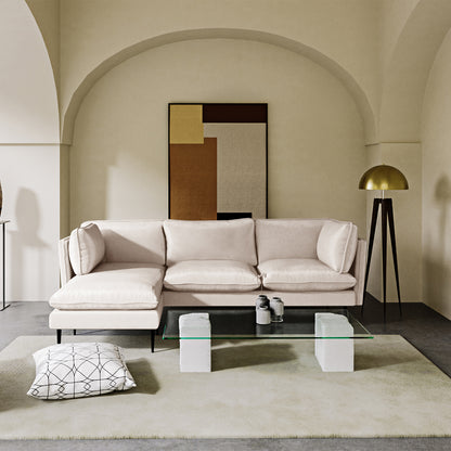Erling 3 Seater Velvet Sofa with Chaise – Cream, featuring plush velvet upholstery and sleek steel legs, positioned in an elegant indoor setting with modern decor elements like a tripod lamp and abstract painting.