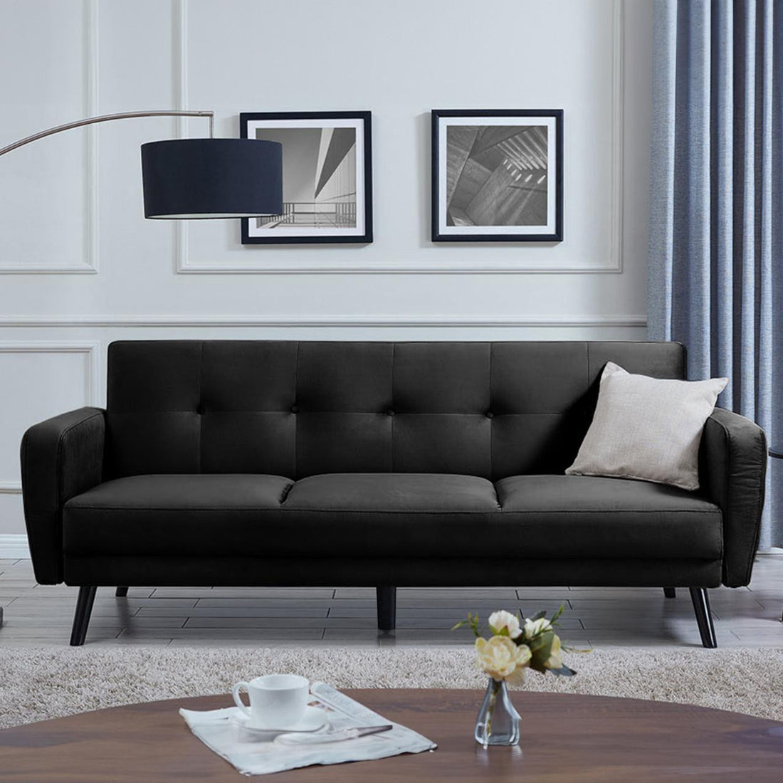Esben 3-Seater Velvet Sofa Bed - Black on display, showcasing its sleek design with rolled arms and wooden legs on a black couch, highlighting its stylish and modern appeal.