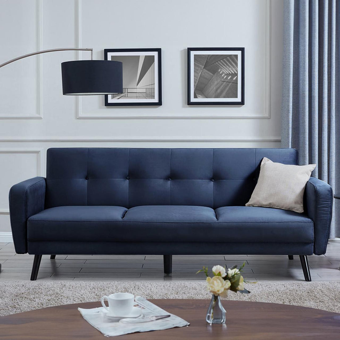 Esben 3-Seater Velvet Sofa Bed - Navy Blue on a blue couch features sleek rolled arms, thick cushions, and wooden legs, combining elegance and functionality for versatile modern living spaces.