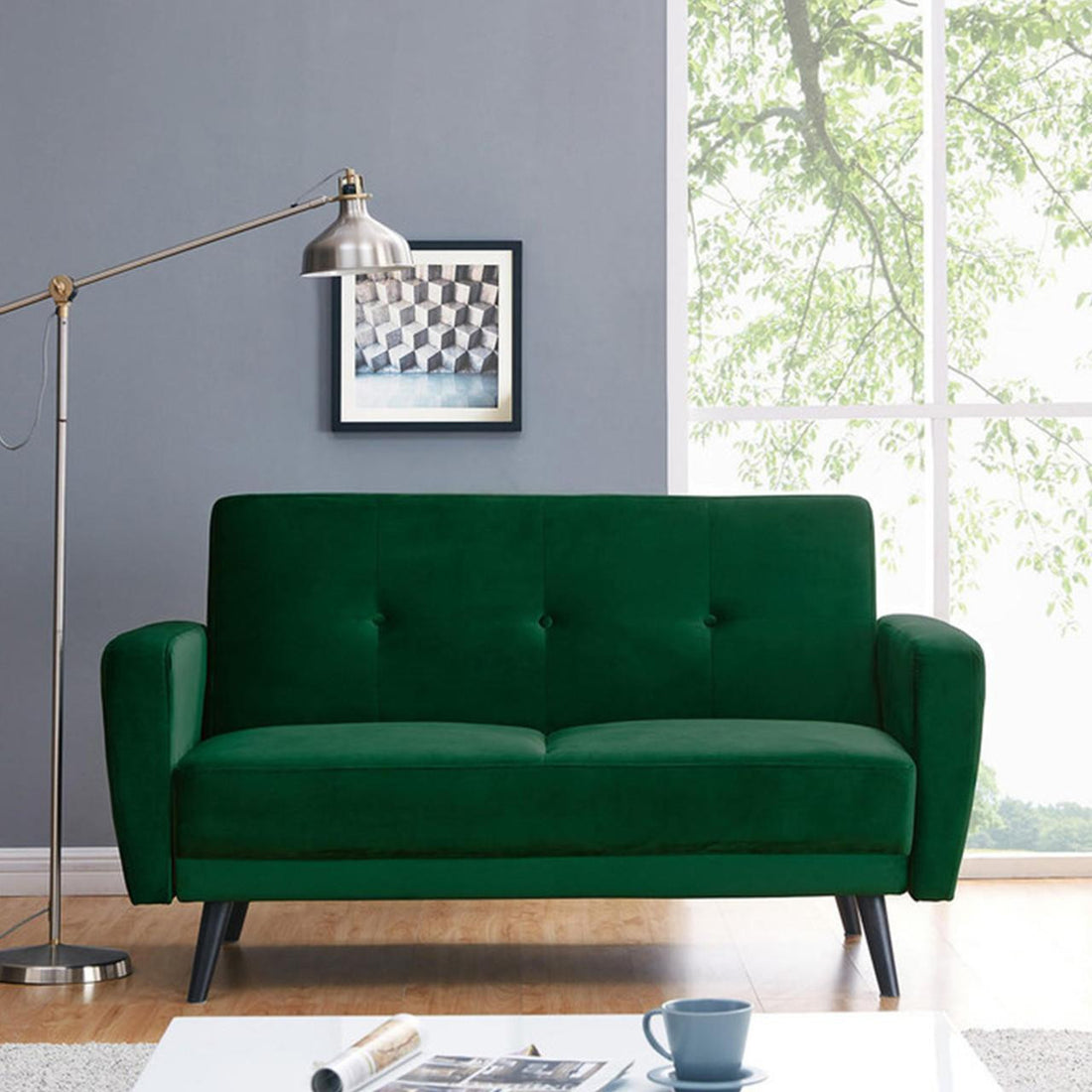 Esben 2-Seater Velvet Sofa Bed in Forest Green, features rich tufted panels, black tapered legs, and is paired with a sleek metal lamp, abstract artwork, and light-wood flooring for a modern living space.