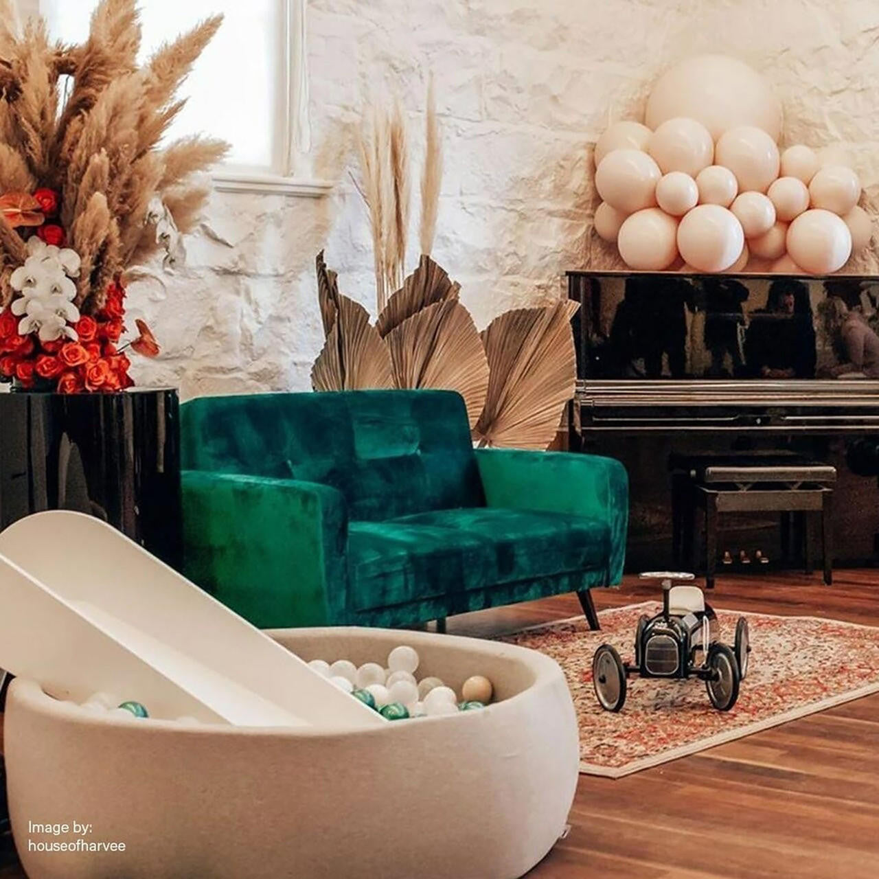 The Esben 2-Seater Velvet Sofa Bed in Forest Green appears plush and stylish, set against a whitewashed brick wall, complemented by elegant kid-friendly elements like a ball pit and vintage toy car.