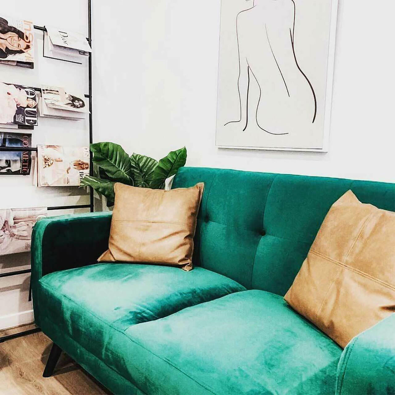 Esben 2-Seater Velvet Sofa Bed in Forest Green, featuring button-tufted back and angled wood legs, complemented by tan pillows, minimalist artwork, and a black magazine rack in a contemporary setting.