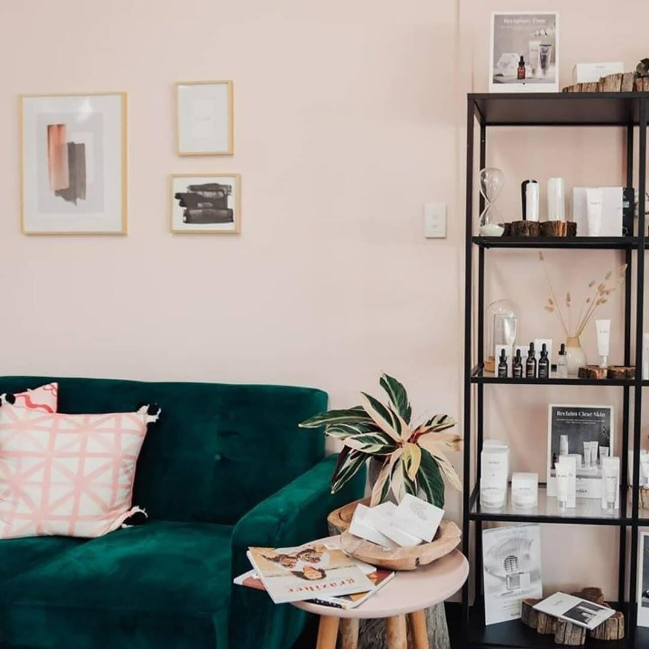 Esben 2-Seater Velvet Sofa Bed in Forest Green featured in a serene lounge, paired with a geometric-patterned cushion, beside a pink side table with magazines and a leafy plant.