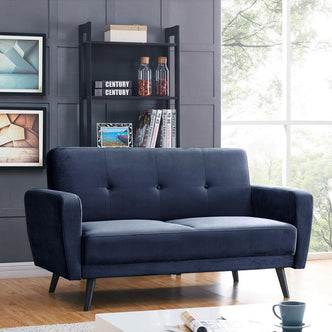 Navy blue Esben 2-Seater Velvet Sofa Bed with slim black legs, set in a modern living room, featuring a low white coffee table and dark shelving unit with decorative items.