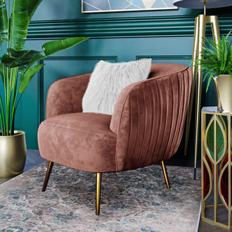 Evelyn Curved Velvet Sofa Accent Chair in Blush with brass legs and a white faux-fur pillow, set against a teal wall, showcasing elegance and mid-century modern design in a stylish interior setting.