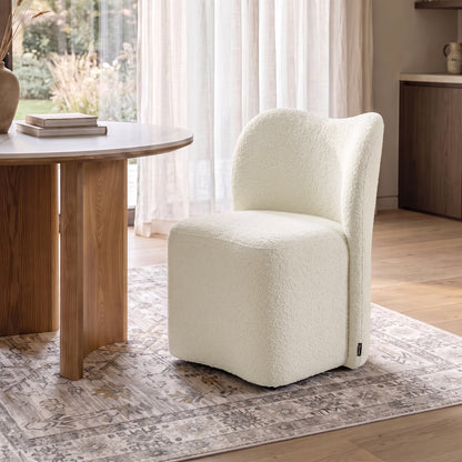 Cream bouclé upholstered swivel dining chair with a high backrest, set at a wooden table in a dining room.   