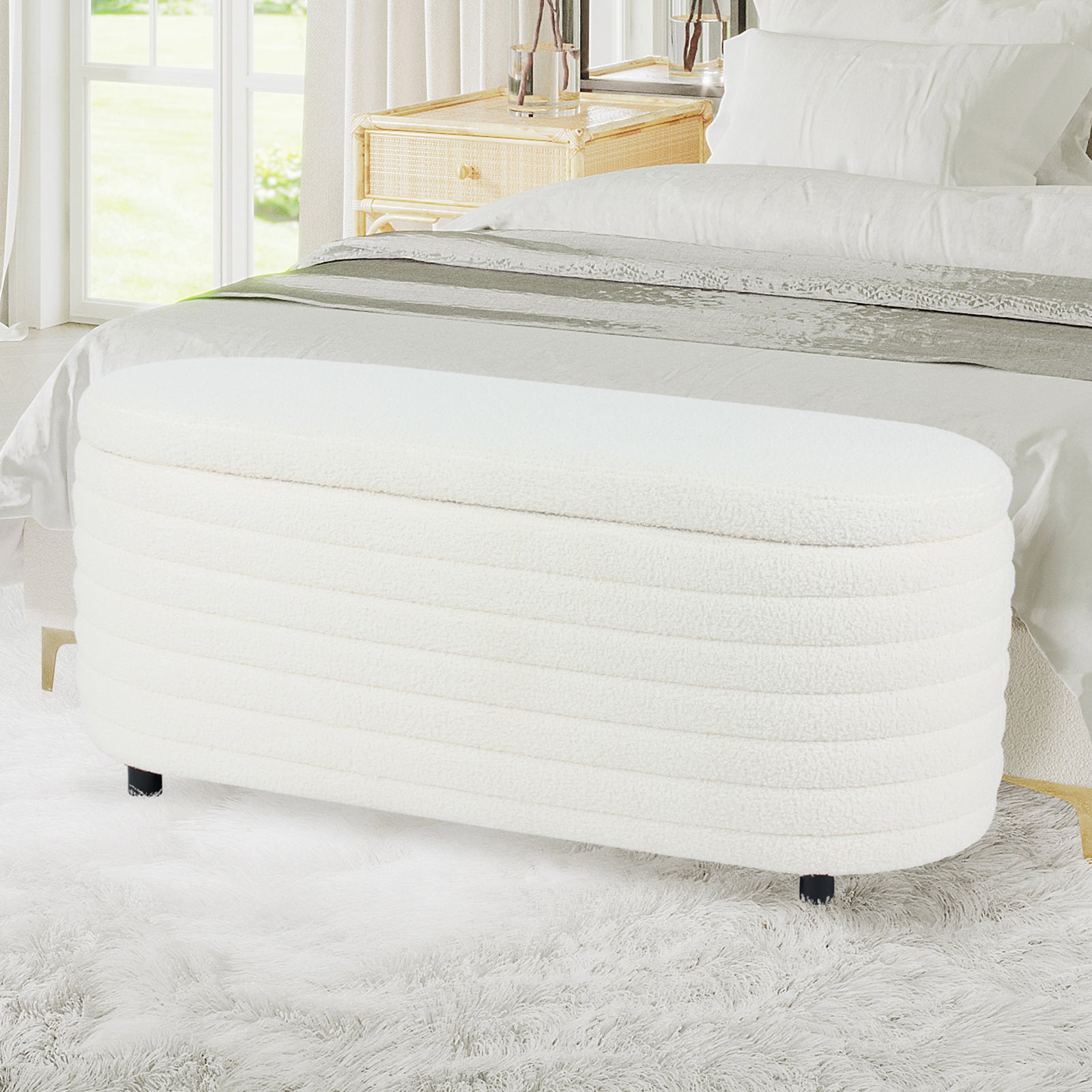 Hartwin 114cm Boucle Ottoman with Storage in Cream White, upholstered in soft bouclé fabric, with short black feet, situated in a bright bedroom, in front of a bed with white linens.