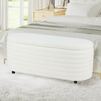 Hartwin 114cm Boucle Ottoman with Storage in Cream White, upholstered in soft bouclé fabric, with short black feet, situated in a bright bedroom, in front of a bed with white linens.