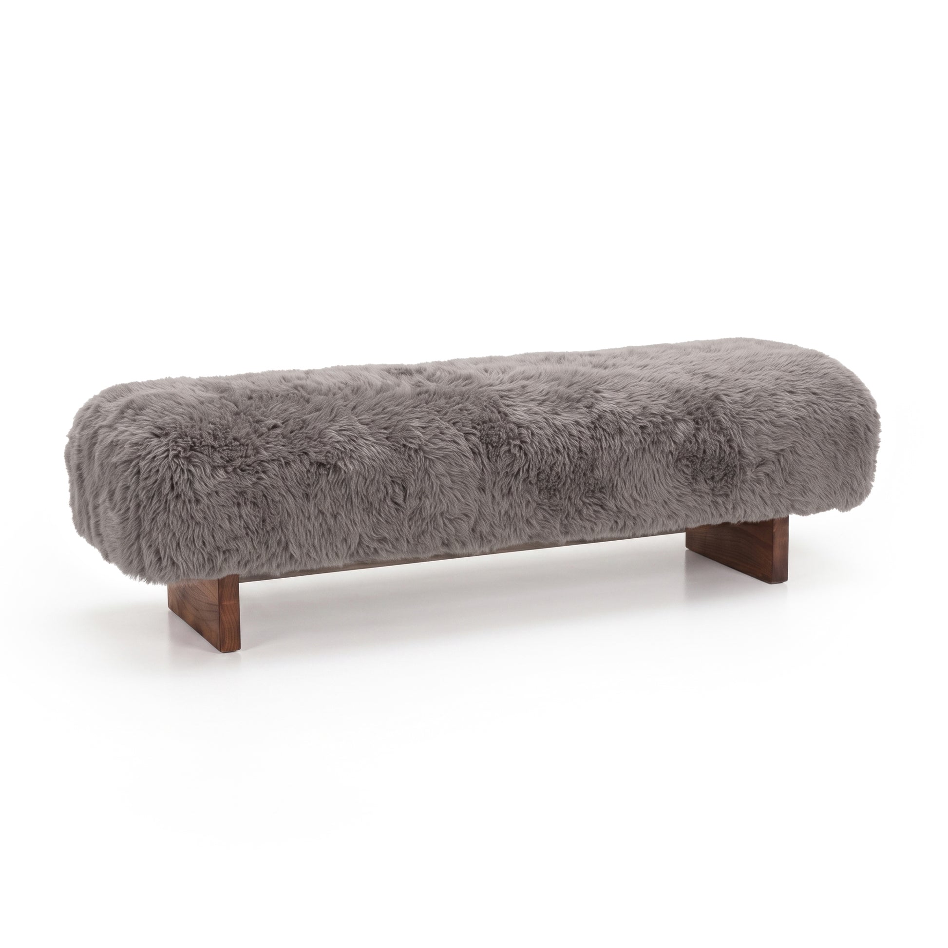 An angled, front-facing view of the taupe faux-fur or sheepskin upholstered bench, highlighting its plush, long-pile texture and low dark wooden block legs against a clean white background.