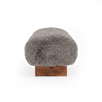 A profile, end-on view of the taupe faux-fur or sheepskin upholstered bench, showcasing its rounded edge profile and low dark wooden block leg against a clean white background.