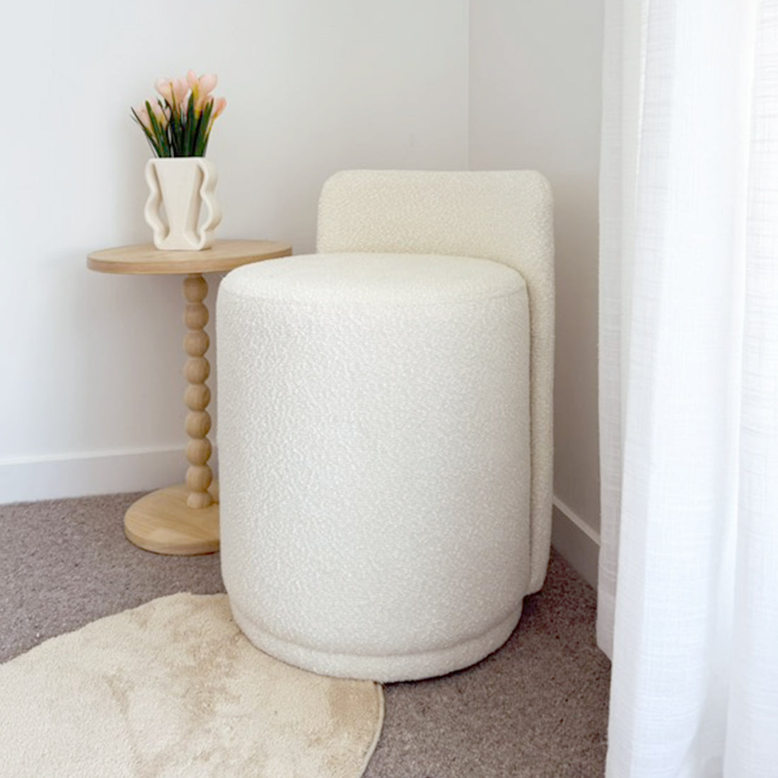 Hiboa Bouclé Ottoman Stool in Eggshell White, a rounded, cream-bouclé upholstered seat with a built-in backrest, complements a Scandinavian-inspired nook with a light-wood table and tulip-adorned vase.