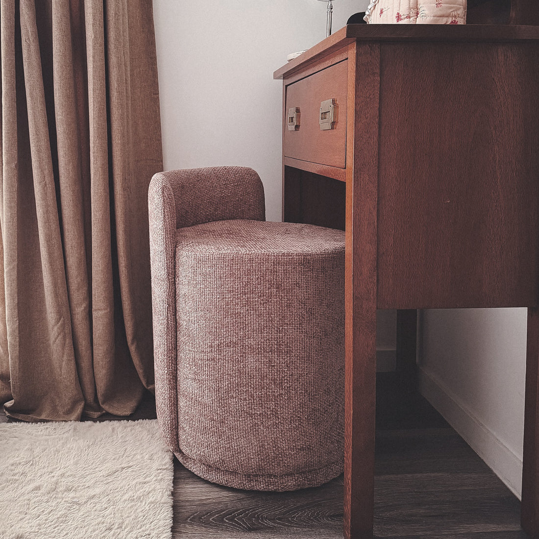 Hiboa Chenille Ottoman Stool in Light Pink, a small, round upholstered stool under a mid-century wooden desk, complemented by neutral drapes and a light area rug on dark wood flooring.