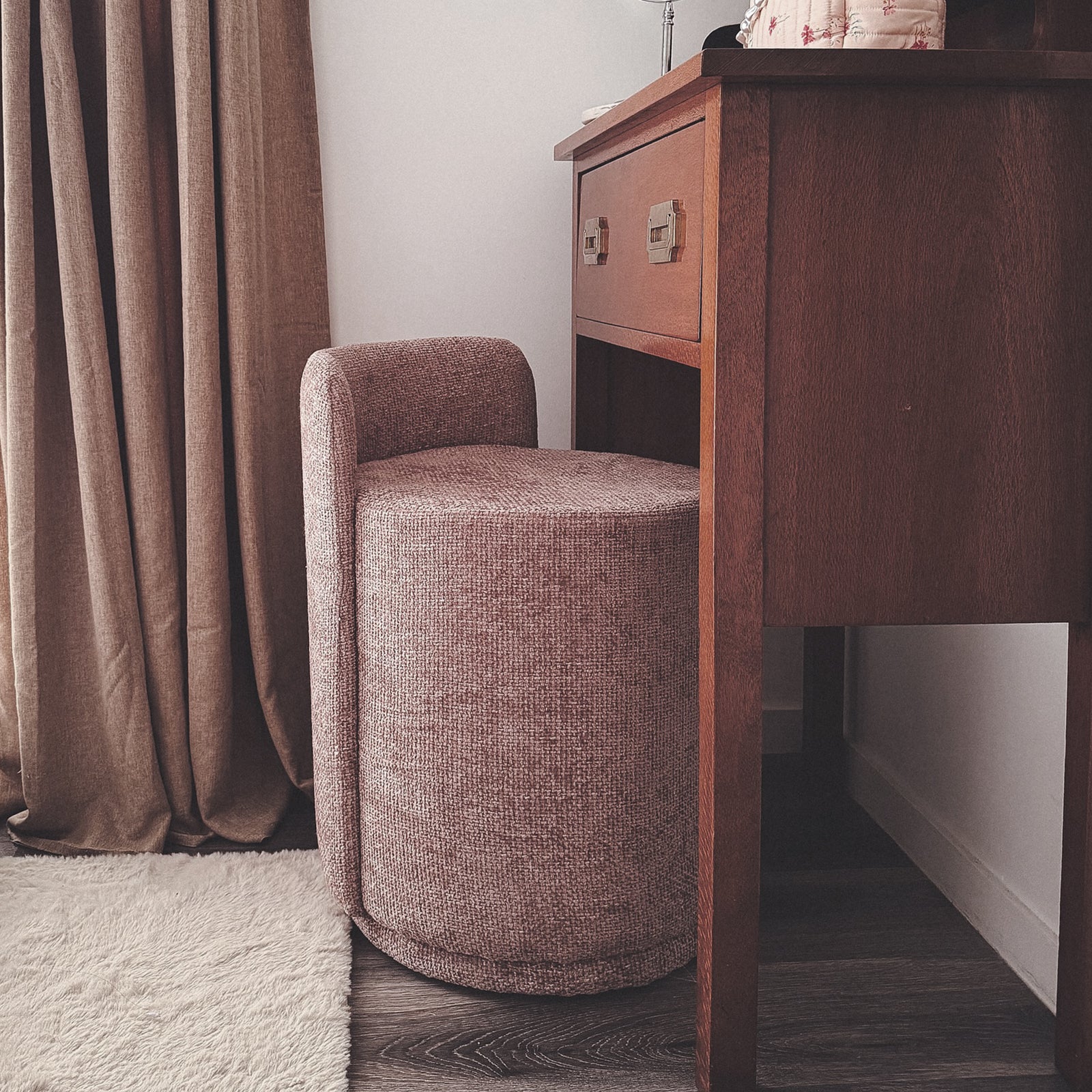 Hiboa Chenille Ottoman Stool in Light Pink, a small, round upholstered stool under a mid-century wooden desk, complemented by neutral drapes and a light area rug on dark wood flooring.